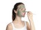Young woman applying clay mask on her face against white background