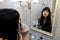 Young woman applying mascara in front of a mirror. Girl getting ready with her makeup in a hotel bathroom. Pretty female serious