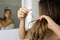 Young woman applying oil mask to hair tips in front of a mirror. Haircare concept. Focus on hair