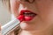 Young woman is applying red shiny lipstick oh her lips