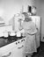 Young woman in an apron in her kitchen tasting her food from a pot