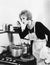 Young woman in an apron in her kitchen tasting her food from a pot