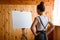 Young woman artist stands in front of easel with canvas on it.