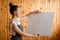 Young woman artist stands in front of easel and holds the canvas with her hands