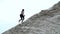 Young woman athlete climbs a sandy mountain. On the background can be seen cargo cranes, cargo port, dawn.