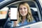 Young woman in auto shows smartphone with blank screen.