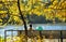 Young woman with a baby carriage sitting on a bench in the autumn park on the banks of the river with yellow autumn leaves on the