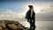 Young woman with a backpack climbing the slippery cliffs at the sea coast at sunset. A concept of adventure, winter tourism, and