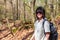 A young woman with a backpack enjoys a walk through a peaceful and lush forest on a sunny day.