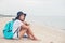 Young woman with backpack sitting on lonely beach and looking in