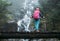 Young woman with backpack and trekking poles enjoying power mountain river waterfall on wooden bridge during Makalu Barun National