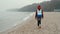 Young Woman with Backpack is Walking along Sea Sand Beach in Fog Autumn Day