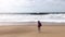 A young woman with a backpack walks the ocean shore