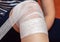 A young woman bandages a bandage on her injured knee. Self-help in case of a knee injury. Injured or injured knee, bruised knee