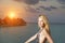 The young woman in a bathing suit at sunset on background of the sea and silhouettes of houses over water