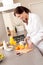 Young woman in bathrobe cutting orange in kitchen