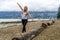 Young woman at the beach of Stanley Park stands barefoot on log,