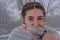 Young woman with beautiful green eyes wears scarf in winter outdoors. Lady froze snow, snowflakes in her hair. Close-up