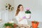 A young woman in a beige hoodie and purple rubber gloves replants indoor plants in new pots.