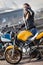 Young woman biker wearing neck face mask standing next to street bike outdoor