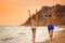 Young woman in bikini and her  walking on beach at sunset. Lovely couple