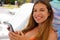 Young woman in bikini holding smartphone and looking at camera. Beautiful girl using mobile phone at beach. Smiling brunette woman
