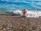 A young woman in a bikini sits on a pebble Konyaalti Beach among the waves