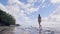Young woman in bikini walking on wet sand on sea beach on sky an palm tree view. Beautiful girl in swimsuit on ocean
