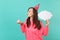 Young woman in birthday hat blowing out candle on cake, holding empty blank Say cloud, speech bubble for promotional