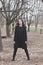 Young woman in black dress and coat stand in park full body shot front view winter
