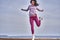 Young woman with black hair jumps while jogging. A woman is engaged in gymnastics in the spring morning on the sandy bank of a lar