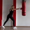 Young woman in black sportswear in stylish sneakers in red boxing gloves beats a punching bag in a modern gym. Girl in training