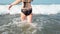 Young woman in black swimsuit spends time in sea. Adult lady swims towards the waves.