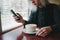 A young woman in black uses the phone in a cafe and drink coffee with marshmallows.