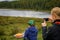 Young woman blogger takes a photo of her friend from behind against mountain lake. Tourist picnic on the background of beautiful