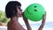 young woman blowing inflating a green balloon, young female on the beach. Ocean, Bali, Indonesia.