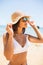 Young woman in blue bikini wearing white straw hat enjoying summer vacation at beach. Portrait of beautiful latin woman relaxing a