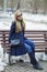 Young woman in a blue coat sitting on a bench in winter park