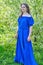 A young woman in a blue dress stands tall in a spring park