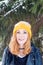 Young woman with blue eyes and blond hair in a yellow knitting hat under the fir tree at the moment of