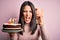 Young woman with blue eyes holding birthday cake with candles over pink background annoyed and frustrated shouting with anger,