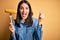 Young woman with blue eyes holding fork with fresh cob corn standing over yellow background screaming proud and celebrating