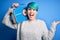 Young woman with blue fashion hair listening to music holding vintage portable radio very happy and excited, winner expression