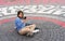 Young woman in blue sweatshirt uses smartphone while sitting on street cobbled square