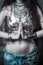 Young woman in boho style shiny top and massive necklace with hands in yoga mudra gesture namaste greating outdoor summer