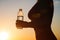 Young woman with bottle water after jogging on the sunset backgrounds. Top view on the city