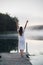 Young woman breathe deep while standing on a wooden pier on a sunrise in the morning at foggy lake