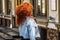 Young woman with bright long red hair on a city street.