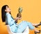 Young woman brunette in blue official suit and high heel shoes sitting in designer armchair with pineapple on yellow