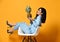 Young woman brunette in blue official suit and high-heeled shoes sitting in designer armchair with pineapple on yellow